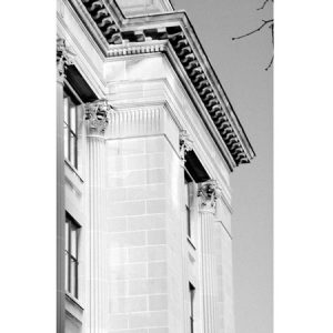 black and white photograph of top of old building with columns and ornate details