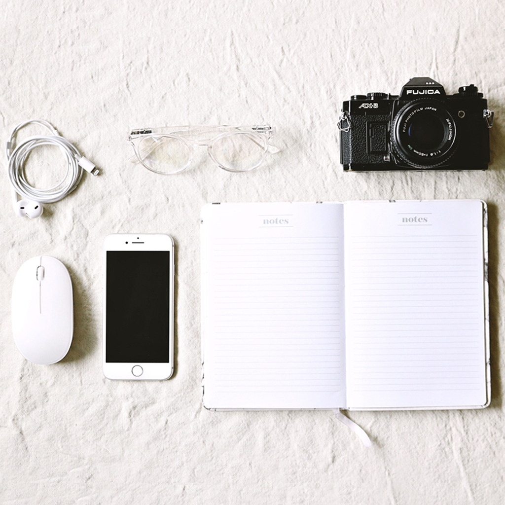 Photo of camera, notebook, phone, glasses, phone cable, and mouse