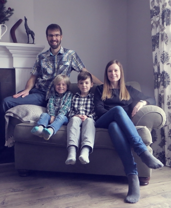 Family picture on couch together. Surrounded by floral curtains and fireplace.