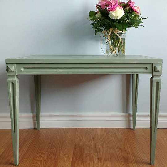 Green end table with pink, white flowers in vase on top