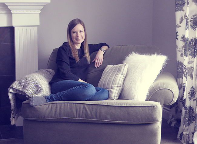 Woman on couch with pillows, floral curtains, and fireplace.